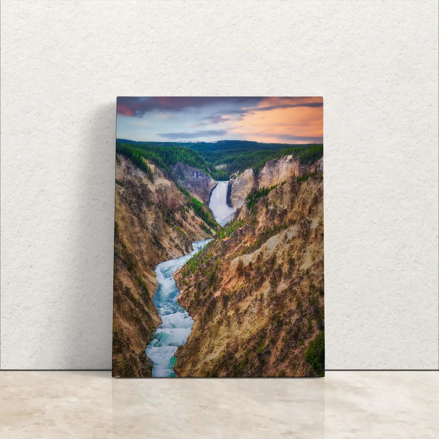 Canvas wall art of Lower Yellowstone Falls at sunset leaning against a white wall, showcasing the vibrant colors and tranquil water flow.