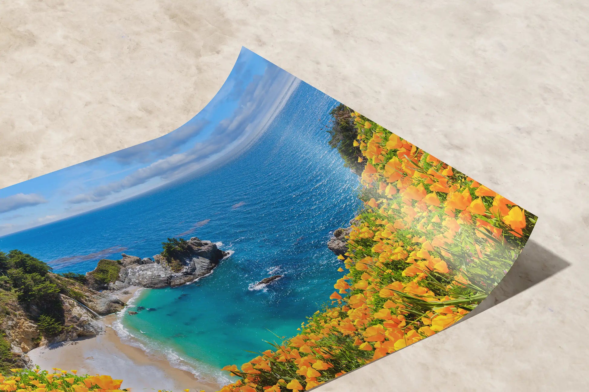 A paper print detail to reveal a vibrant image of McWay Falls at Big Sur with bright yellow flowers in the foreground on a table.