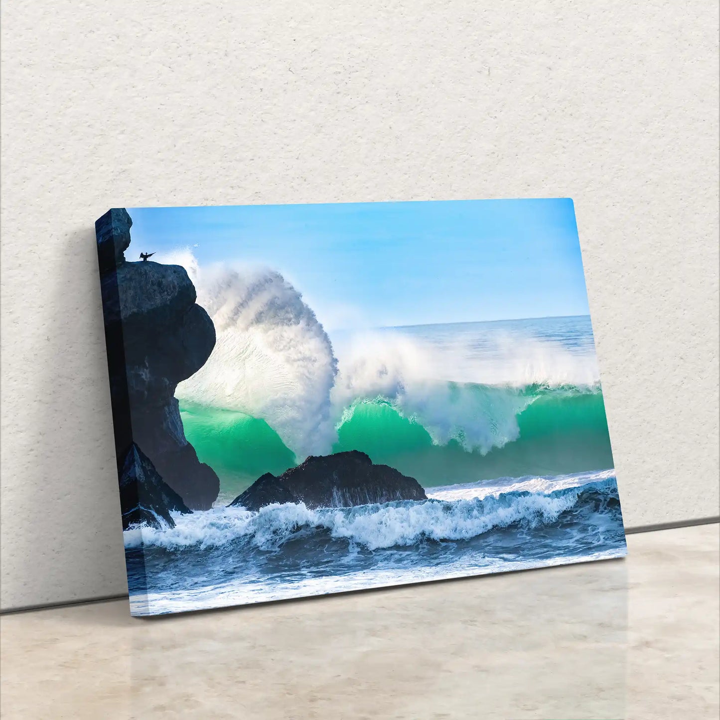 Leaning canvas print of a massive ocean wave near Morro Rock, with vivid colors and a dynamic spray, against a white wall.