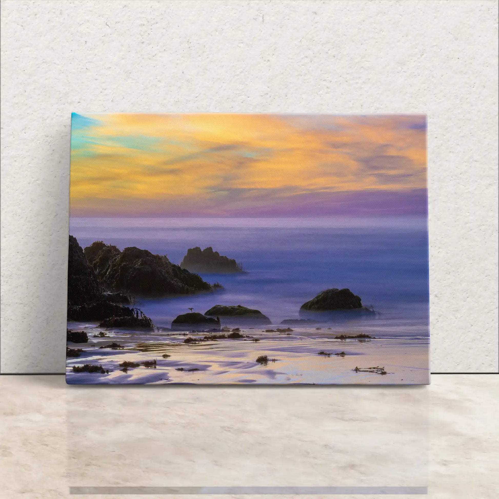 Canvas art leaning against a wall, capturing the vivid sunset over Purple Sand Beach in Big Sur, with lavender hues reflecting on the water.