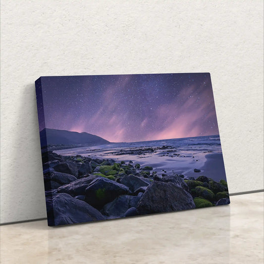 A canvas print resting against a wall, depicting a beach under a starry night sky with purple hues.