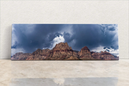 Panoramic canvas wall art featuring the Red Rock Canyon under stormy skies, displayed horizontally and leaning against a white wall.