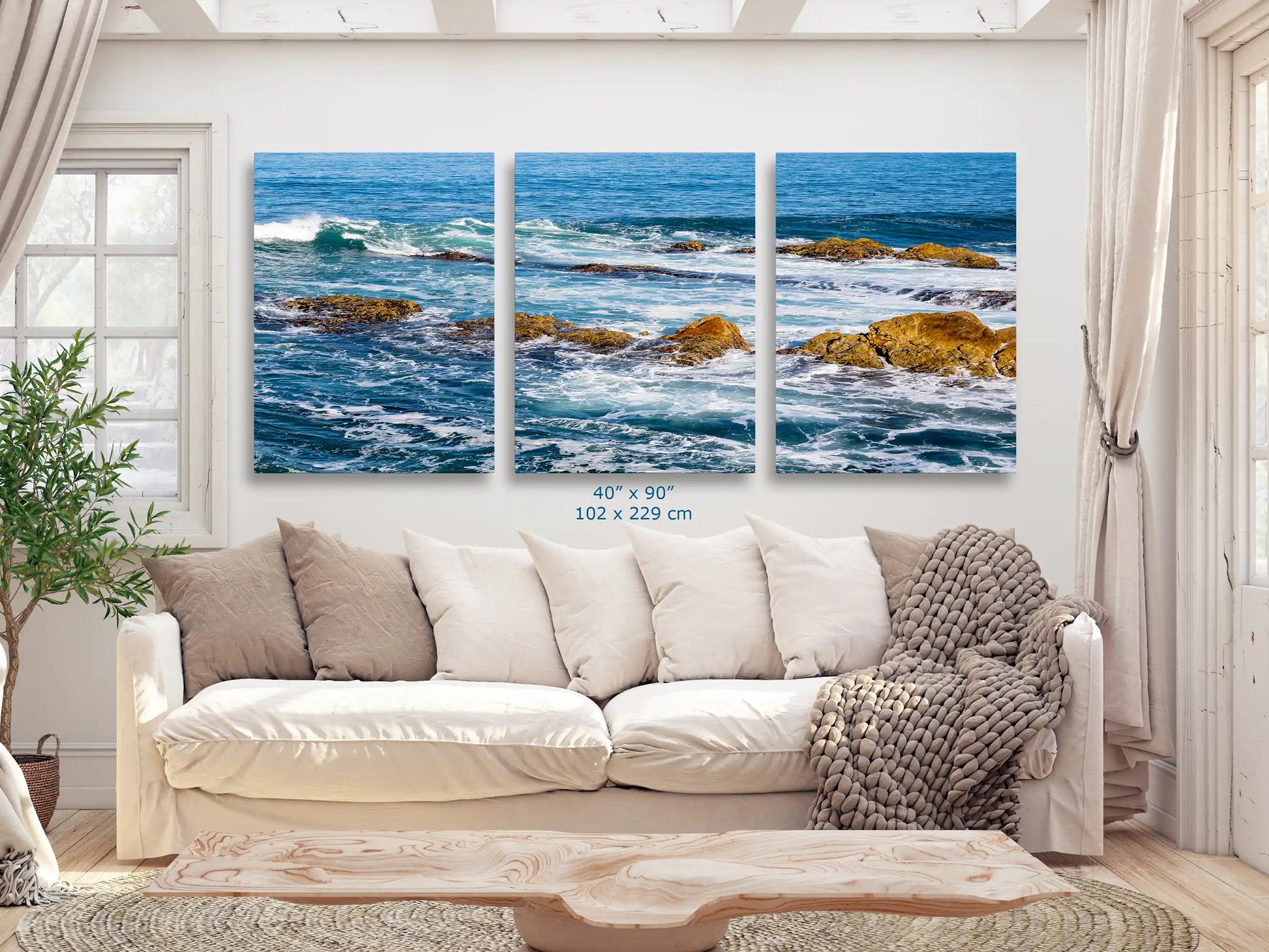 An expansive 40"x90" canvas art set of the ocean scene, divided into three panels, displayed over a large couch in a bright living room.