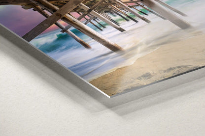 A dynamic angle of metal wall art showing the foamy sea waves and wooden pillars under Balboa Pier at sunset.