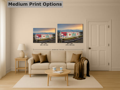 a living room with a beige sofa, a coffee table, and a lamp. Above the sofa, there are two framed prints of a building, likely a stadium, displayed on the wall. The prints are of different sizes, with one being larger than the other. The image also includes text that provides information about the medium print options, such as the dimensions and the standard size of the footprint.
