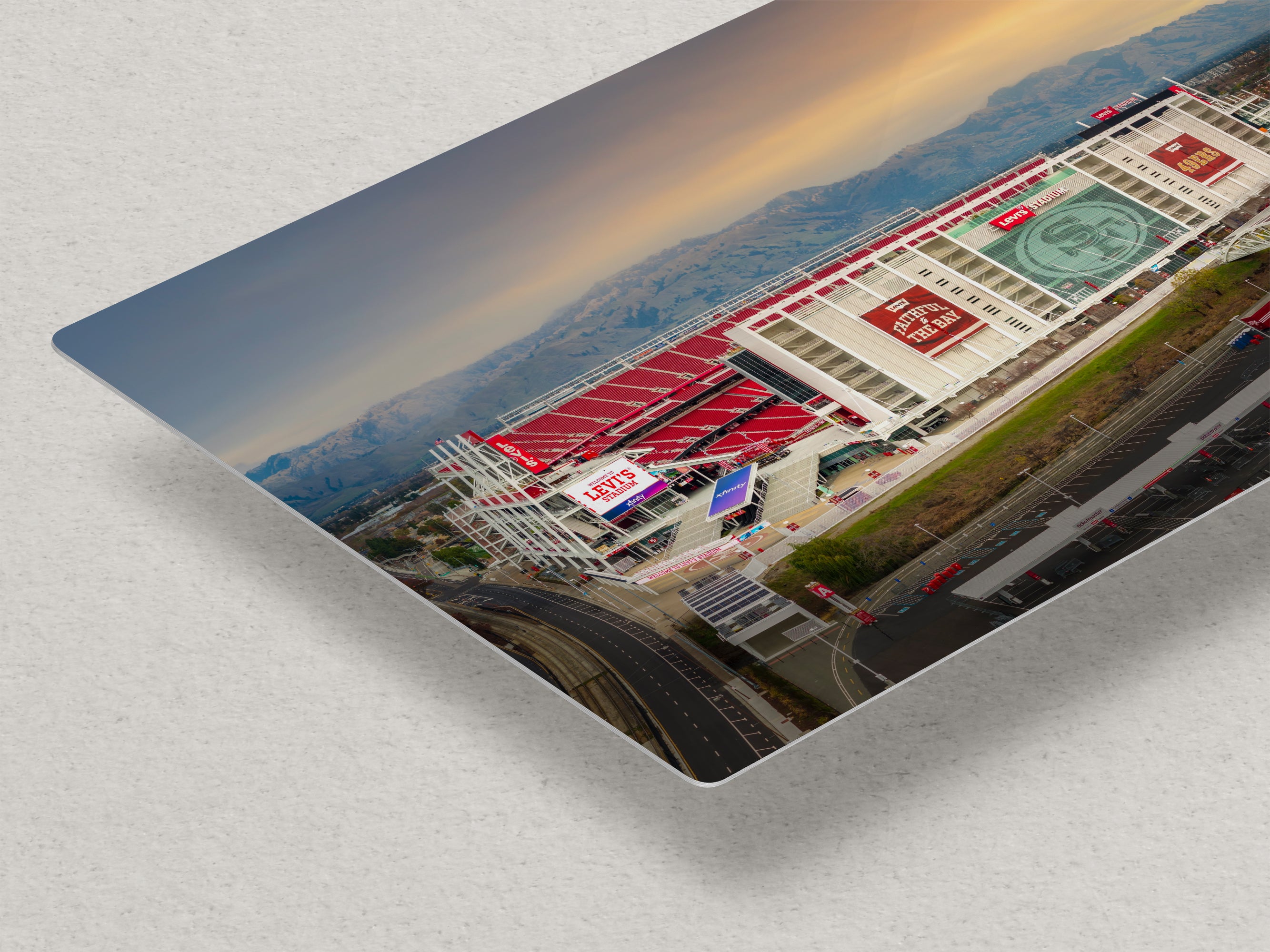 a large stadium with a red roof and various advertisements, set against a mountainous landscape.