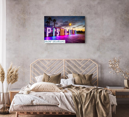 A 24x36 canvas print of the Pismo Beach neon sign displayed in a minimalist bedroom setting with natural tones.