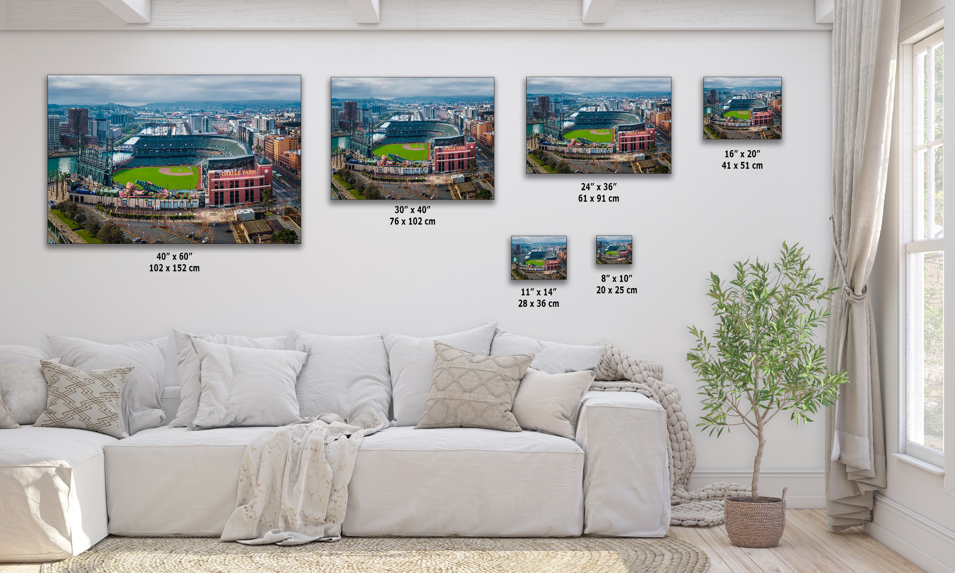 The image is a living room with a white sofa and a potted plant. There are four framed photographs of a baseball stadium displayed on the wall, each with a different size and resolution.