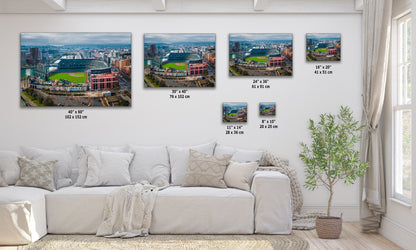 The image is a living room with a white sofa and a potted plant. There are four framed photographs of a baseball stadium displayed on the wall, each with a different size and resolution.